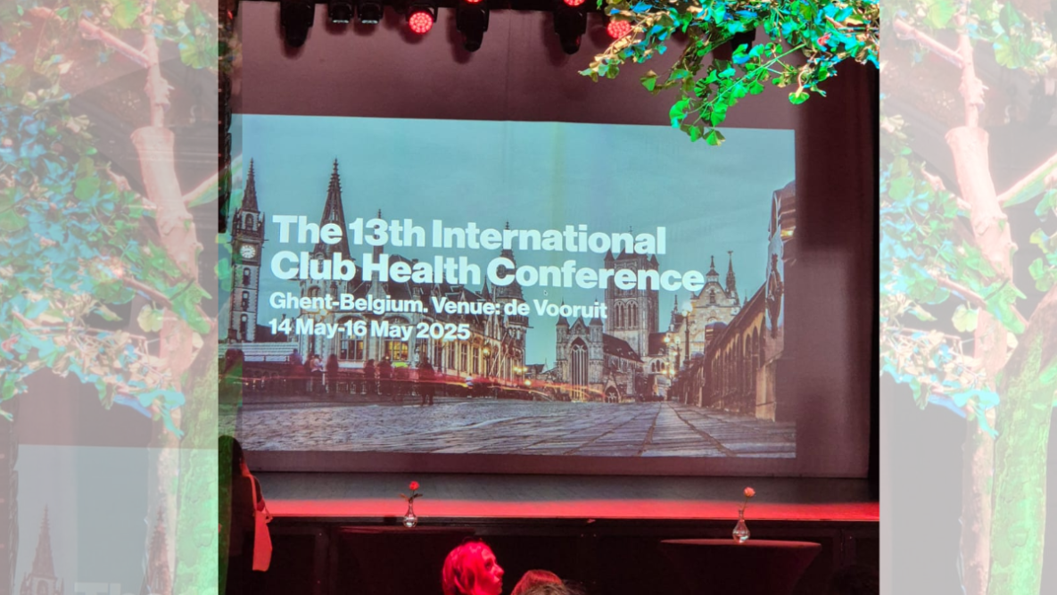 A large projector screen showing a welcome message for the club health conference